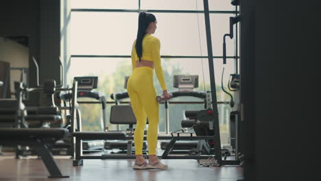 Young-muscular-hispanic-woman-doing-Lunges-exercise-with-dumbbells-in-the-gym-In-yellow-sportswear.-Female-athlete-exercising-with-dumbbells-in-a-lunge-position-at-gym.